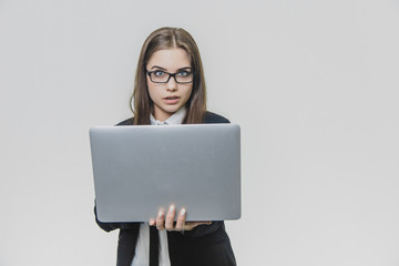 Beautiful young businesswoman is wearing glasses and using a modern computer touchscreen. Confident female employer is working and is concentrated. Girl is looking at the camera. Being shocked she is