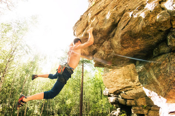 Rock climber climbs bouldering on a cliff on forest. Low angle of strong rock climbing man hanging free on rock with sunflare