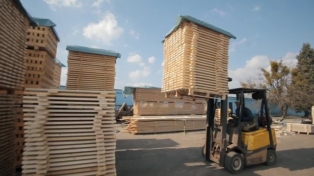 Forklift operator handling wooden pallets in warehouse. Man using loader dor Pack of wooden planks.