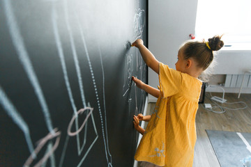 caucasian little girl draws on the wall with chalk - obrazy, fototapety, plakaty