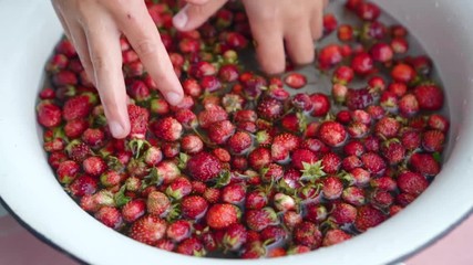 Child shows to the camera strawberries in his hands and put it back to water