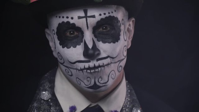 Close up of a smiling man dancing, wearing a hat and face painted as a skull, 4k