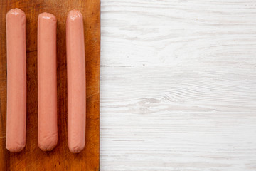 Hot dog sausages on a rustic wooden board over white wooden background, top view. Flat lay, overhead, from above. Copy space.