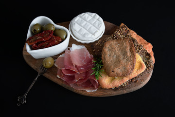 still life crispy pizza, prosciutto, soft cheese, green olives, dried tomatoes on wooden plate. Isolated on black background.
