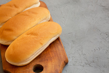 Hot dog buns on a rustic wooden board on a concrete surface, low angle view. Copy space.