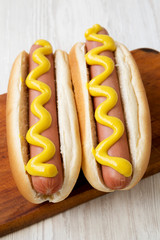 Hotdog with yellow mustard on a rustic wooden board on a white wooden background, low angle view....