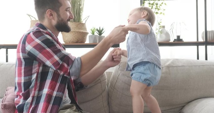 Father With Cute Baby Daughter Dancing On Sofa