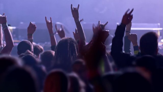 Unrecognizable fans dancing at a concert or festival party. Silhouettes of concert crowd in front of bright stage lights. UHD, 4K , slow motion