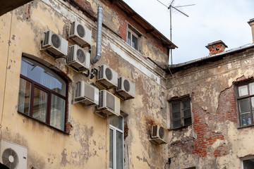 air conditioners on the crumbling brick facade of an old house with windows and falling plaster. gloomy industrial cityscape