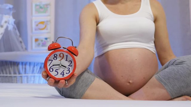 Future mother in the final month of pregnancy. A pregnant woman holds a clock in hand, symbolizes quickly passing nine months of pregnancy, conceptual countdown to delivery