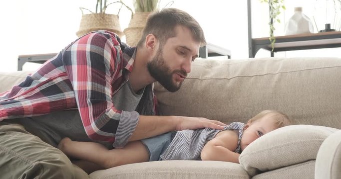 Father caressing baby daughter lying on sofa