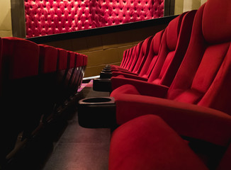 Red cinema velvet seats with low lighting & copy space - Movie theatre chairs with cupholders - Film premiere auditorium with seating ready for audience - Entertainment, lifestyle & enjoyment concept