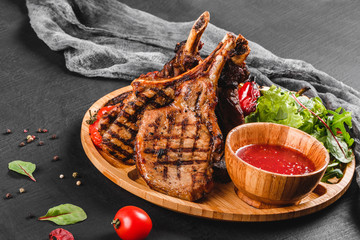 Grilled Ribeye Steak on bone and vegetables with fresh salad and bbq sauce on cutting board over...