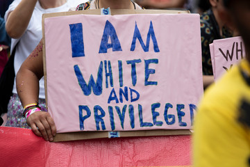 A person holding an I am white and privileged banner at a gay pride event - obrazy, fototapety, plakaty