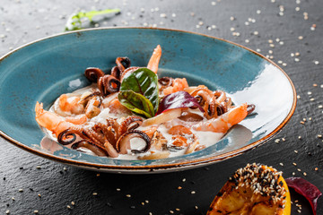 Fried prawns, mussels, calamari, cuttlefish, octopus with cream sauce in plate on dark stone background. Clean eating, healthy food concept. Seafood platter. Top view