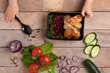 girl holding black food school container with dinner, top view. Children lunch box