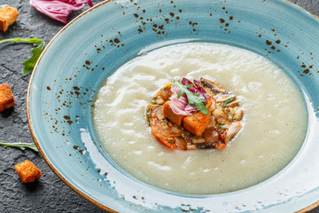 Cream soup of celery with tartare from baked vegetables decorated from croutons and arugula in plate on dark stone background. Top view, Flat lay. Vegetarian food