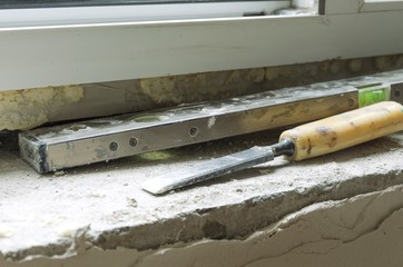 Builder`s tools. Old spirit level and chisel on the stone window sill