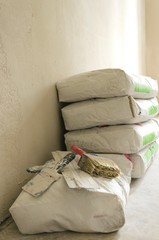 Stack of cement bags on the floor against wall and builder`s tools.Process of repair.Vertical shot