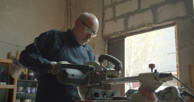 Senior male master works at wood factory pressing the headsaw cutting the wood.
