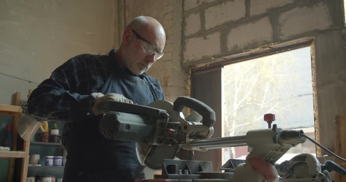 Senior male manufacturer working at wood with headsaw cutting being concentrated and serious.