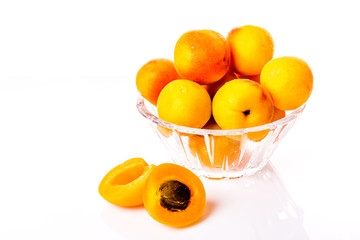Ripe and bright apricots on a glass plate with water droplets and one apricot cut with a bone.