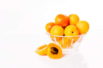 Ripe and bright apricots on a glass plate with water droplets and one apricot cut with a bone.