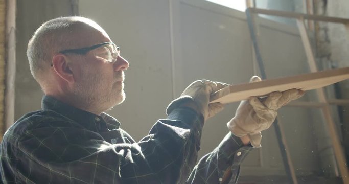 Portrait of senior carpenter checks the quality of a wooden board in manufacture.