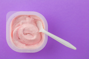 Yogurt cup with strawberry yogurt and with white plastic spoon dipped isolated on purple background