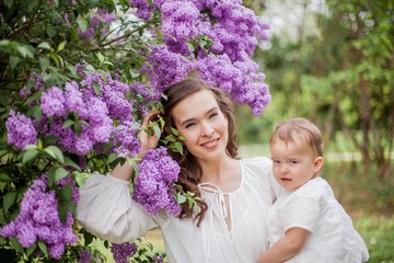 Beautiful young mother and daughter near the blossoming lilac. Spring.