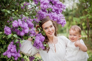 Beautiful young mother and daughter near the blossoming lilac. Spring.