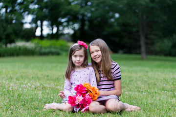 Horizontal full length view of cute fair smiling pre-teenager with arm around a small girl sitting...