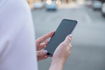 Beautiful brunette business woman in white skirt and grey suit trousers working on a mobile phone in her hands outdoors. European city on background. copy space