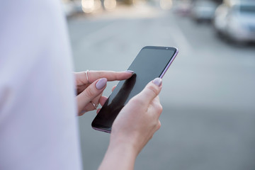 Beautiful brunette business woman in white skirt and grey suit trousers working on a mobile phone in her hands outdoors. European city on background. copy space