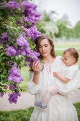 Beautiful young mother and daughter near the blossoming lilac. Spring.