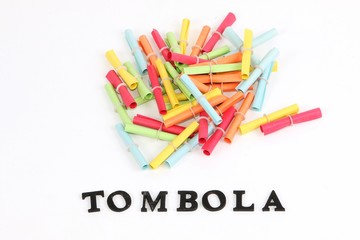 heap of colorful tombola tickets are lying in the white studio with a word tombola in the front with wooden letters