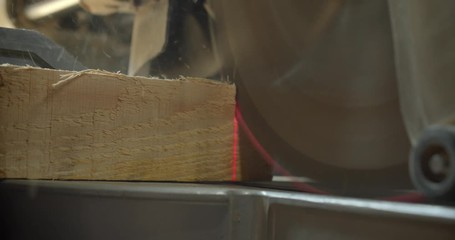 Close-up shot of a piece of wood being cut with an electric cut off saw at manufacture.