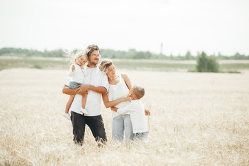 An Happy family of four having fun in the wheat field on sunny summer day.