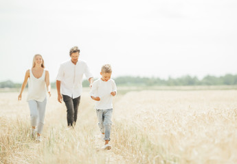 Happy family of three walk in wheat field in sunny summer day