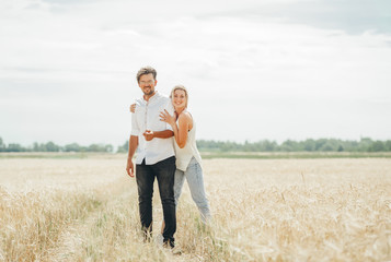 Naklejka na ściany i meble Young happy pretty sunny couple is standing fashion and smiling on the spikelets in the field background