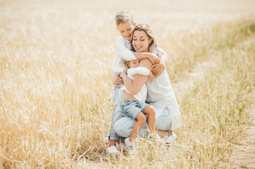 Mom hugging and loving her little kids in wheat field. Happy mother and her children spending time together outdoors