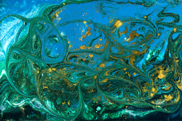 Liquid uneven blue and green marbling pattern with golden glitter and glare of light