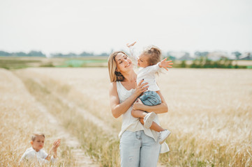 Mother holding a little smiling girl at the wheat field. Mother with children outdoors