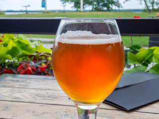 View of full beer glass from side on wooden table, outdoors with beautiful view in daylight lots of bubbles, beer has just been poured.