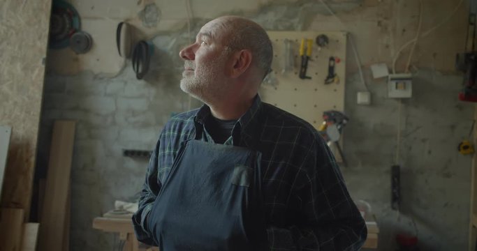 Close-up portrait of senior male carpentry master standing at wood manufacture watching into camera being serious and calm.