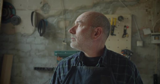 Senior male carpentry master standing at wood manufacture turns to camera being serious and calm.