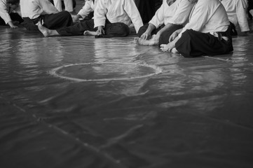 Black and white image of aikido. Men are sporsmen. Aikido workshop. A number of black belt practitioners in traditional uniform, white kimano and black hakama.