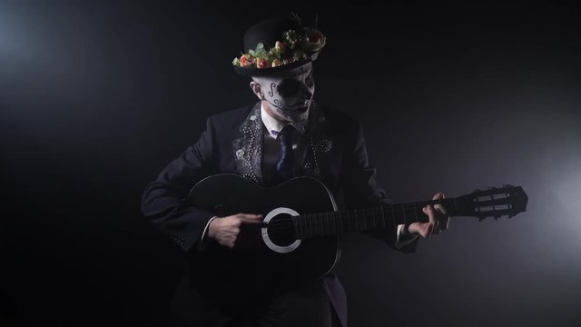 Mexican man in black suit and a hat with flowers is playing the guitar, 4k