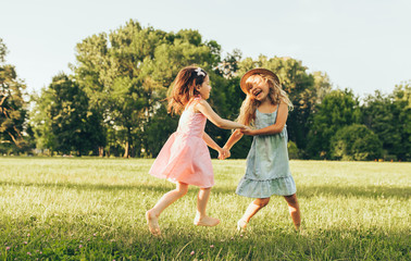 Horizontal image of two little girl dancing on the green grass in the park. Children enjoying...