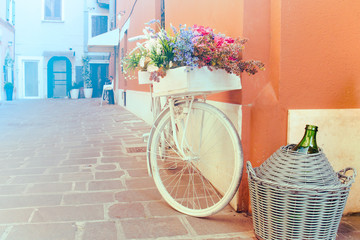 Fototapeta na wymiar Decorative mediterranean bicycle. White bike with flowers and a flask of wine (copy space available on the left)